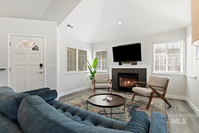 living room with a tiled fireplace, wood finished floors, visible vents, and baseboards