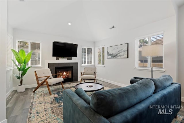 living room with a tiled fireplace, wood finished floors, visible vents, and baseboards