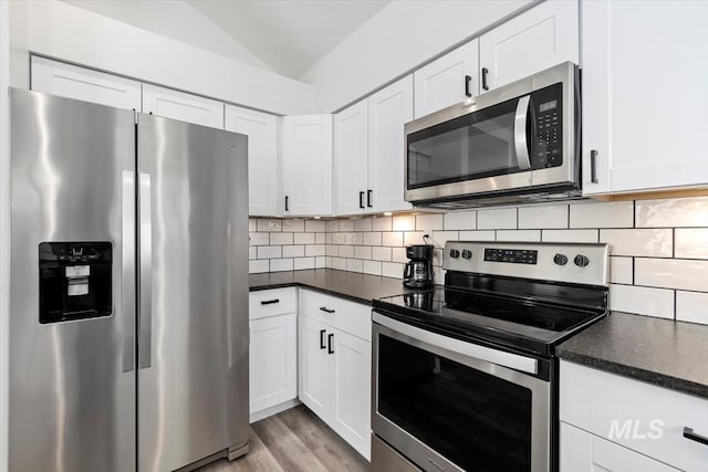 kitchen with lofted ceiling, dark countertops, white cabinets, and appliances with stainless steel finishes