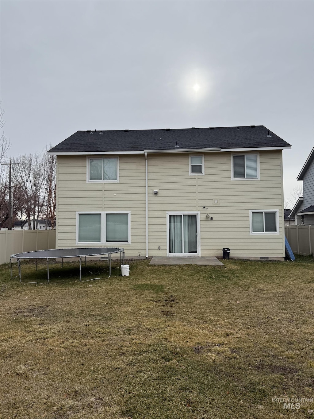 rear view of property featuring a lawn, a patio, and a trampoline