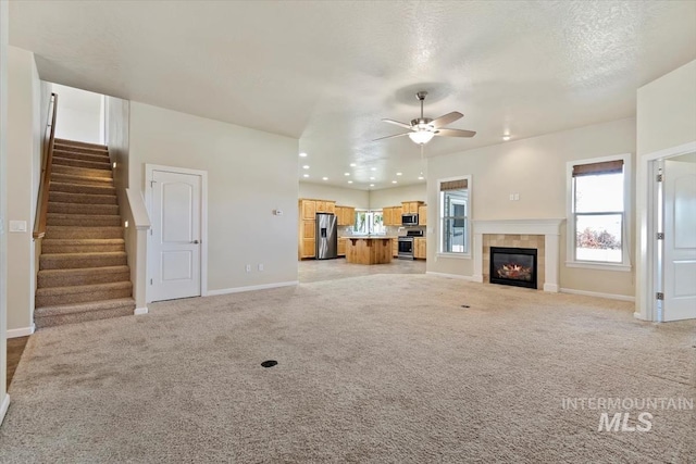 unfurnished living room featuring a fireplace, a textured ceiling, light colored carpet, and ceiling fan