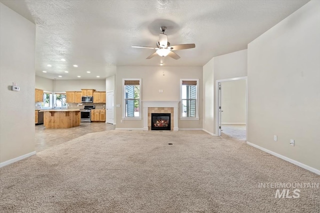 unfurnished living room with light carpet, a textured ceiling, a wealth of natural light, and a tiled fireplace