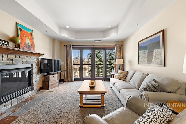 living room featuring a raised ceiling, a stone fireplace, stone tile floors, and recessed lighting