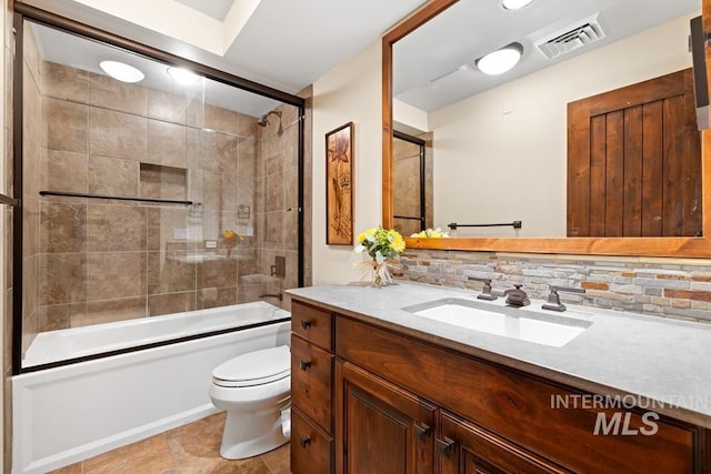 full bathroom featuring tasteful backsplash, toilet, vanity, and shower / bath combination with glass door