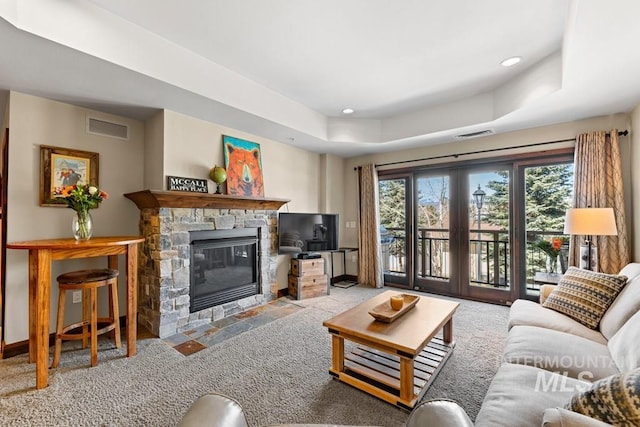 carpeted living area featuring a fireplace, a raised ceiling, baseboards, and recessed lighting