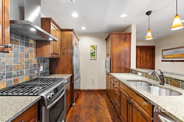 kitchen featuring stainless steel appliances, wall chimney range hood, a sink, light stone countertops, and recessed lighting