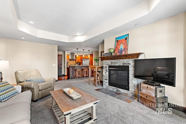 carpeted living area with a raised ceiling, a stone fireplace, and recessed lighting