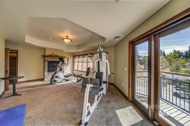 exercise area with a tray ceiling, baseboards, carpet, and a stone fireplace