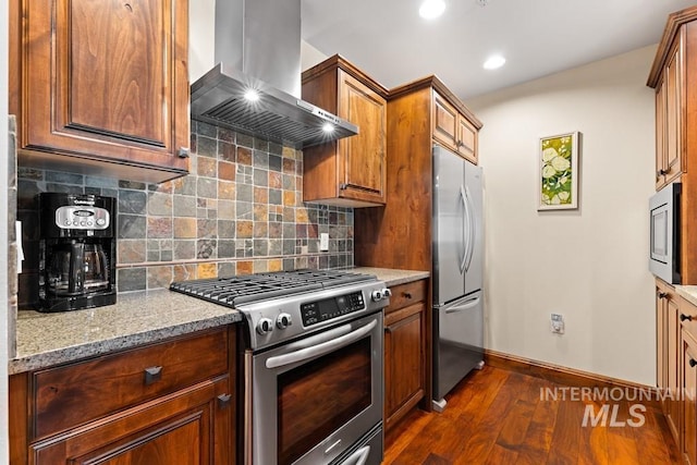kitchen featuring appliances with stainless steel finishes, wall chimney range hood, baseboards, dark wood-style flooring, and tasteful backsplash