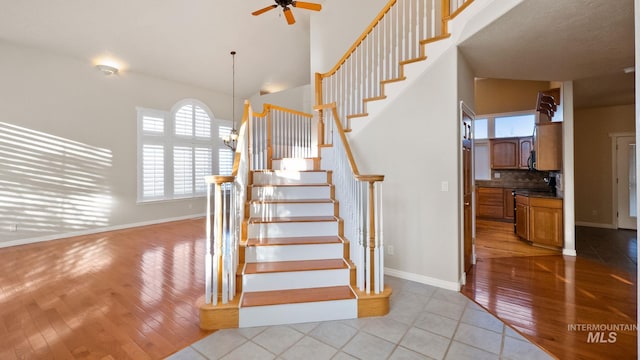 stairs with a towering ceiling, hardwood / wood-style flooring, baseboards, and ceiling fan with notable chandelier