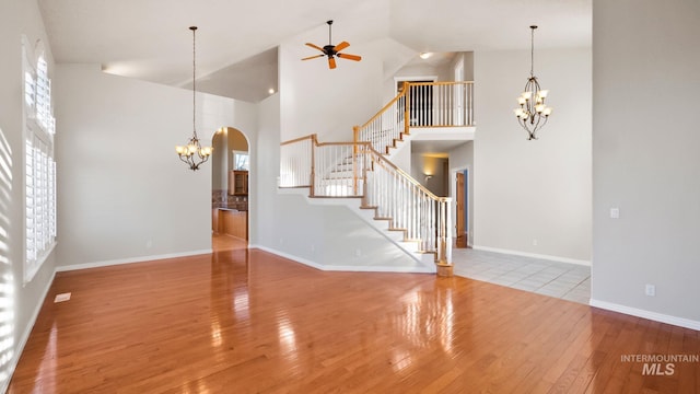 unfurnished living room featuring hardwood / wood-style flooring, stairway, arched walkways, and ceiling fan with notable chandelier