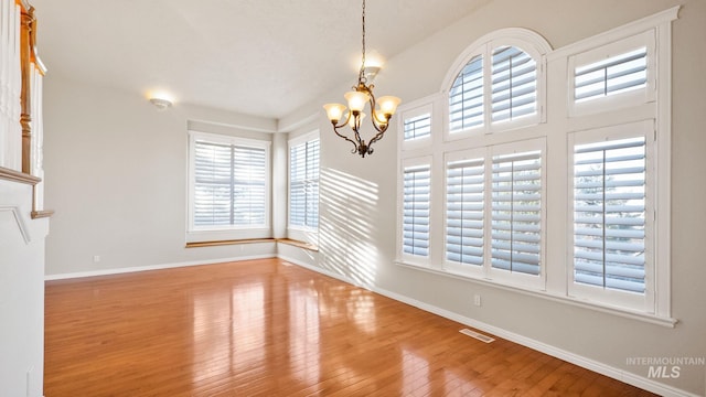 unfurnished dining area with hardwood / wood-style flooring, baseboards, visible vents, and a chandelier