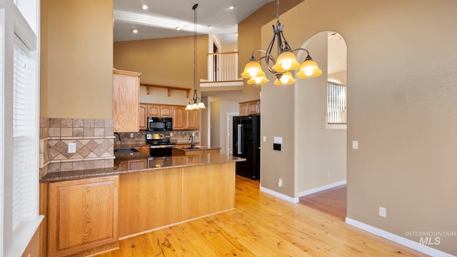 kitchen featuring tasteful backsplash, light wood-style floors, a peninsula, black appliances, and a chandelier