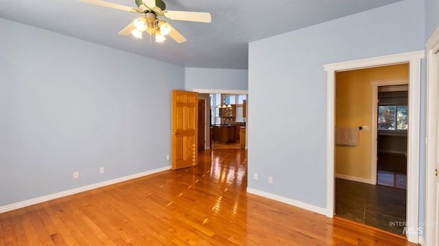 empty room with wood finished floors, a ceiling fan, and baseboards