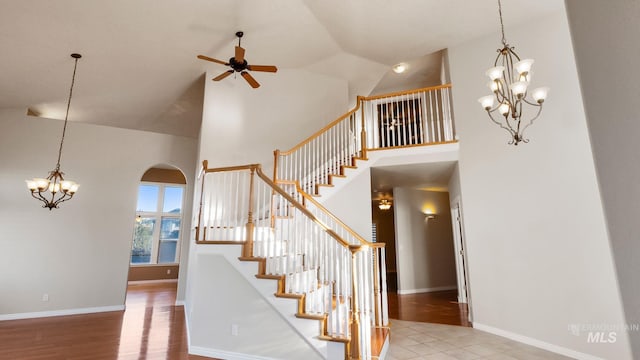 stairway with arched walkways, high vaulted ceiling, wood finished floors, and baseboards