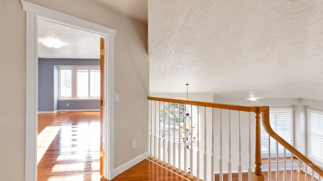 corridor featuring a chandelier, a textured ceiling, baseboards, and wood finished floors