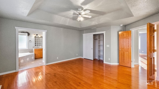 unfurnished bedroom with light wood-type flooring, baseboards, a raised ceiling, and a closet