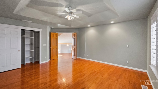 unfurnished bedroom featuring light wood-style flooring, visible vents, a tray ceiling, and baseboards