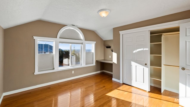 unfurnished bedroom with lofted ceiling, wood-type flooring, baseboards, and a textured ceiling