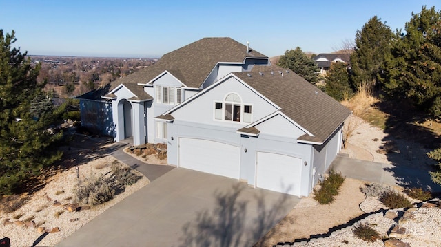 traditional-style house featuring roof with shingles, driveway, an attached garage, and stucco siding