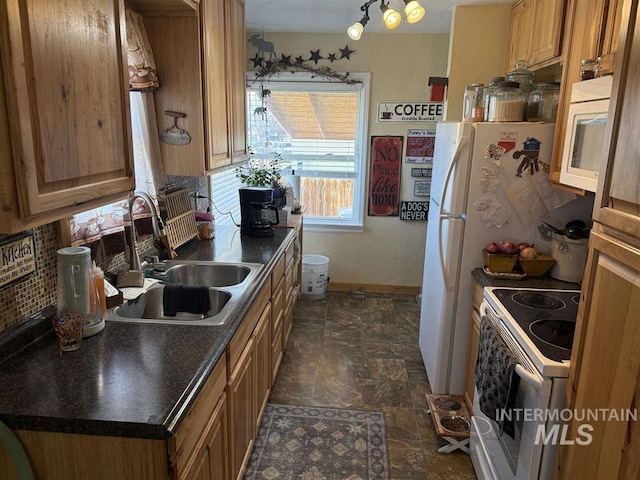 kitchen featuring dark countertops, stone finish floor, a sink, white appliances, and baseboards