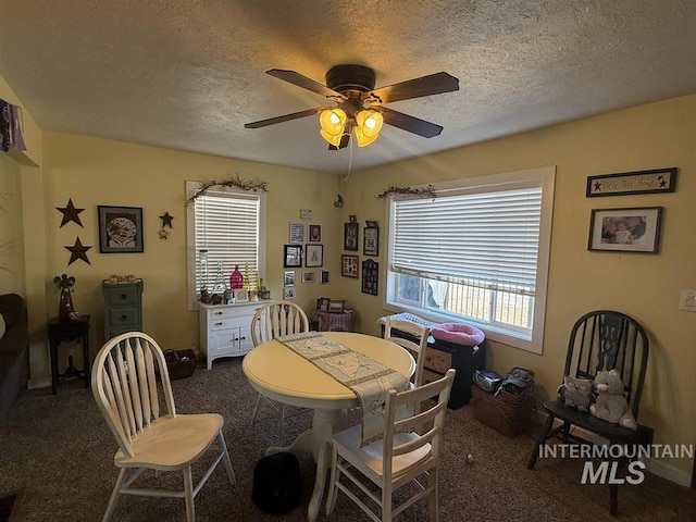 dining space featuring ceiling fan, a textured ceiling, dark colored carpet, and a wealth of natural light