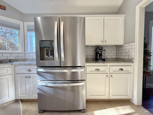 kitchen featuring backsplash, stainless steel refrigerator with ice dispenser, light stone countertops, light tile patterned floors, and white cabinets
