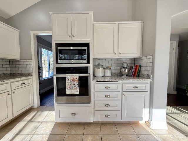 kitchen featuring light stone counters, stainless steel appliances, white cabinetry, lofted ceiling, and tasteful backsplash