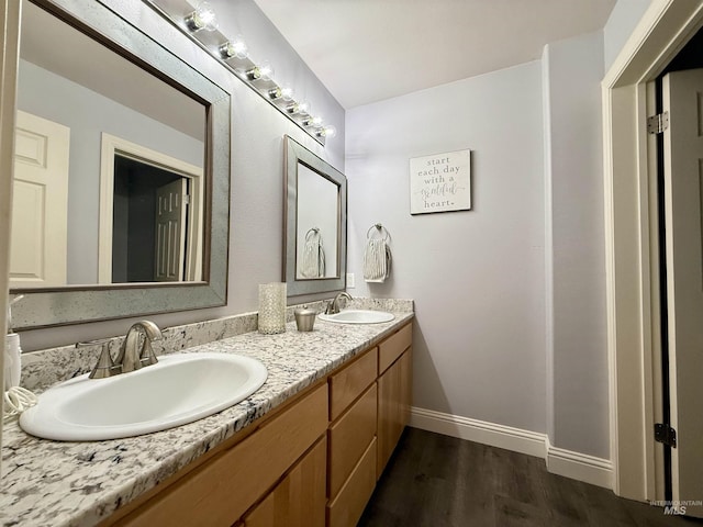 full bathroom featuring a sink, baseboards, double vanity, and wood finished floors