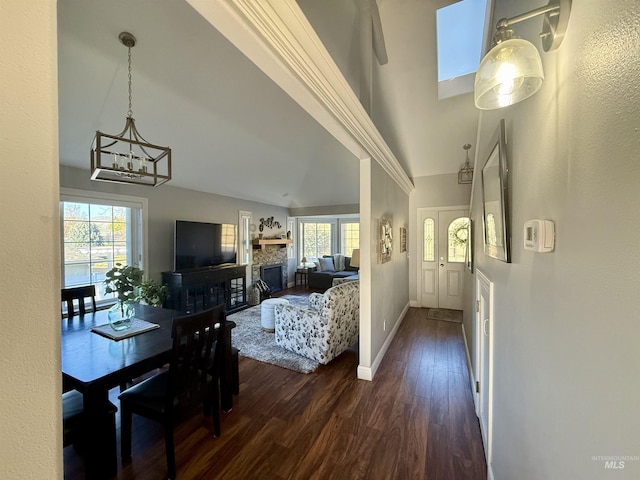 living room featuring baseboards, a stone fireplace, high vaulted ceiling, dark wood-type flooring, and a notable chandelier