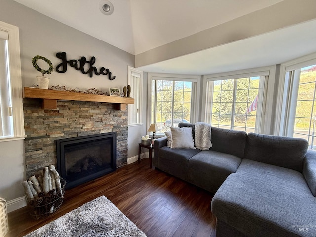 living area with vaulted ceiling, baseboards, a stone fireplace, and wood finished floors