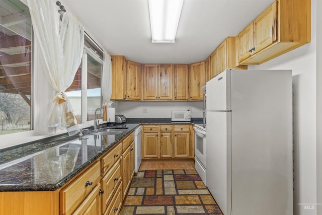 kitchen featuring white appliances, dark stone counters, and a sink