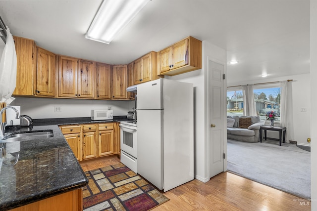 kitchen with white appliances, baseboards, dark stone counters, light wood-style flooring, and a sink