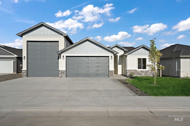 view of front of property featuring board and batten siding, a front lawn, a garage, and stone siding