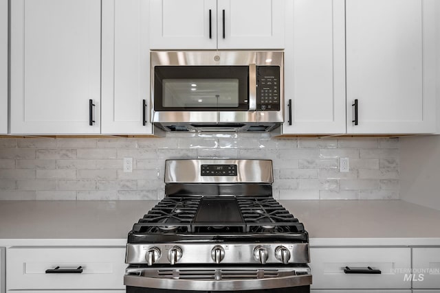 kitchen with tasteful backsplash, white cabinets, stainless steel appliances, and light countertops