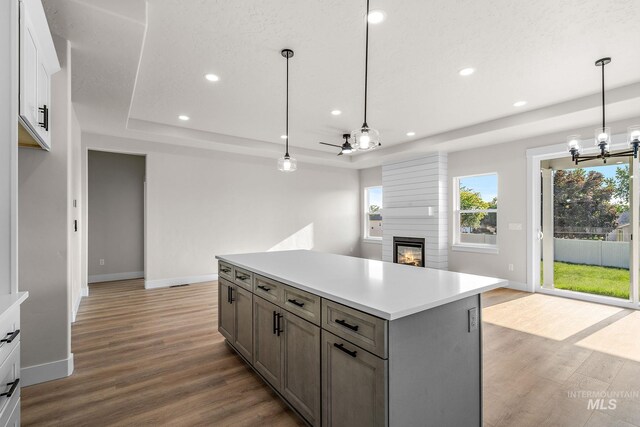 kitchen featuring a tray ceiling, recessed lighting, wood finished floors, and a large fireplace