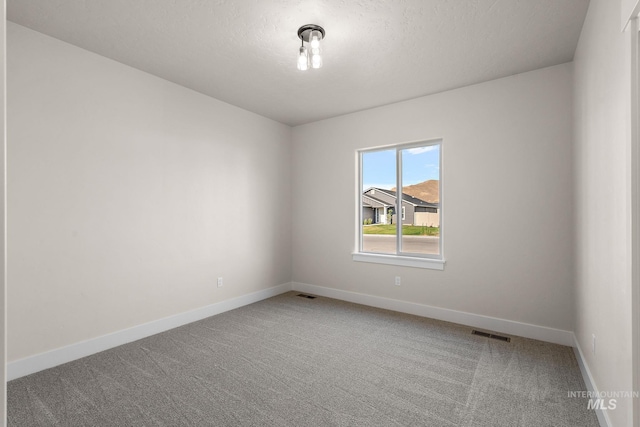 unfurnished room with a textured ceiling, carpet, visible vents, and baseboards