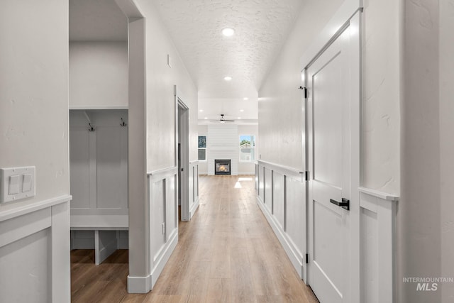 hallway featuring a decorative wall, recessed lighting, a textured ceiling, and light wood-style floors