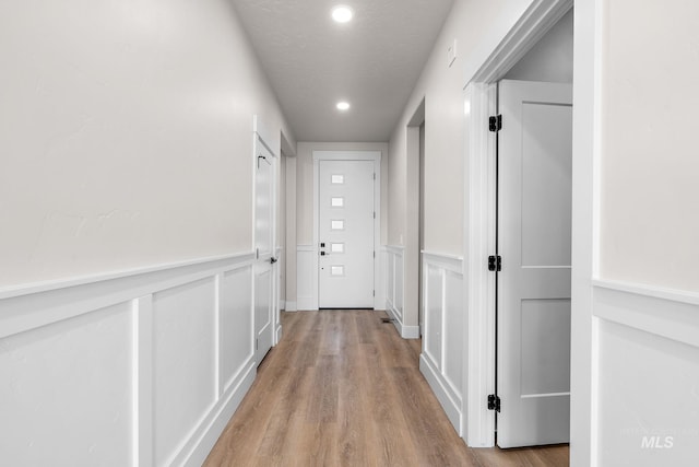 hall featuring a wainscoted wall, recessed lighting, wood finished floors, a decorative wall, and a textured ceiling