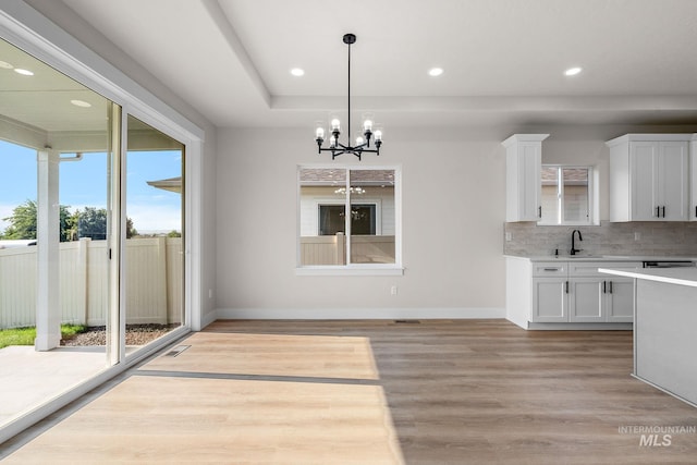 kitchen featuring a sink, backsplash, light wood-style floors, white cabinets, and light countertops