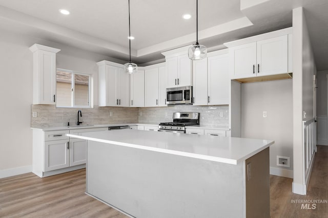 kitchen with a kitchen island, light wood-style flooring, a sink, stainless steel appliances, and white cabinets