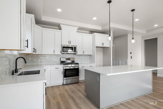 kitchen featuring light wood-type flooring, a sink, stainless steel appliances, white cabinets, and a raised ceiling