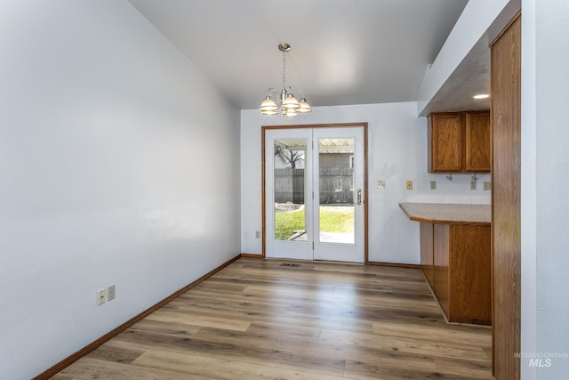 unfurnished dining area featuring an inviting chandelier, baseboards, light wood-style floors, and vaulted ceiling