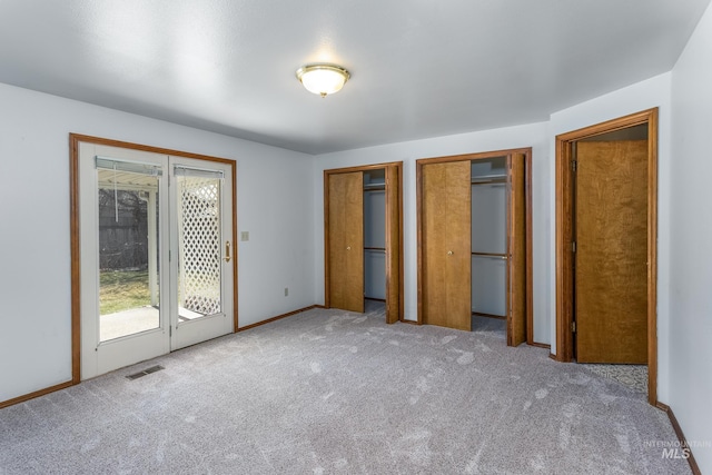 unfurnished bedroom with access to outside, carpet, visible vents, and multiple closets