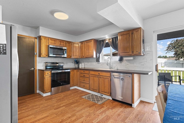 3404 Chukar Ln, Clarkston, WA 99403 - kitchen featuring appliances with stainless steel finishes, a sink, light wood-style floors, decorative backsplash, and brown cabinets