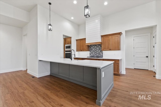 kitchen with appliances with stainless steel finishes, tasteful backsplash, sink, decorative light fixtures, and light hardwood / wood-style flooring