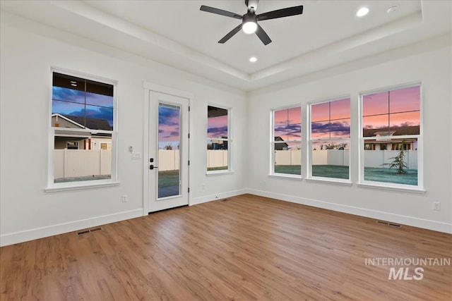 empty room with hardwood / wood-style floors, ceiling fan, and a tray ceiling