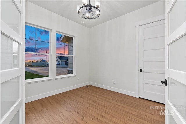 unfurnished room featuring light wood-type flooring and an inviting chandelier