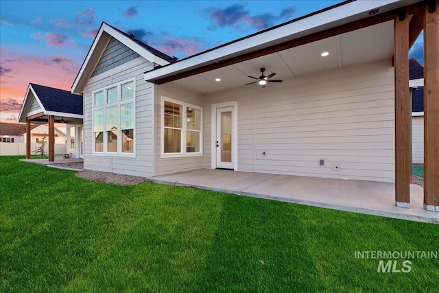 back house at dusk with ceiling fan, a patio area, and a lawn