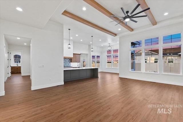 unfurnished living room featuring beamed ceiling, ceiling fan, dark wood-type flooring, and sink